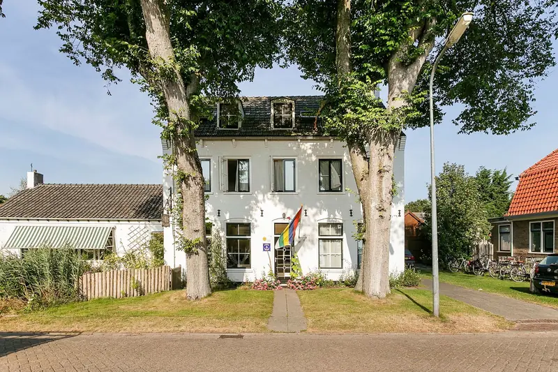 Het witte pand van De Witte Handt tussen twee grote bomen in Midsland