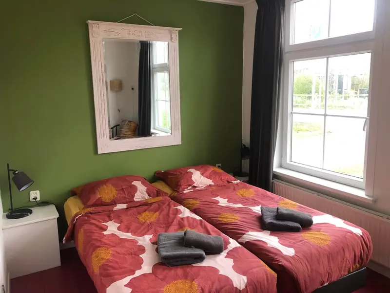 Kamer met een groene wand, twee bedden tegen elkaar en een groot raam