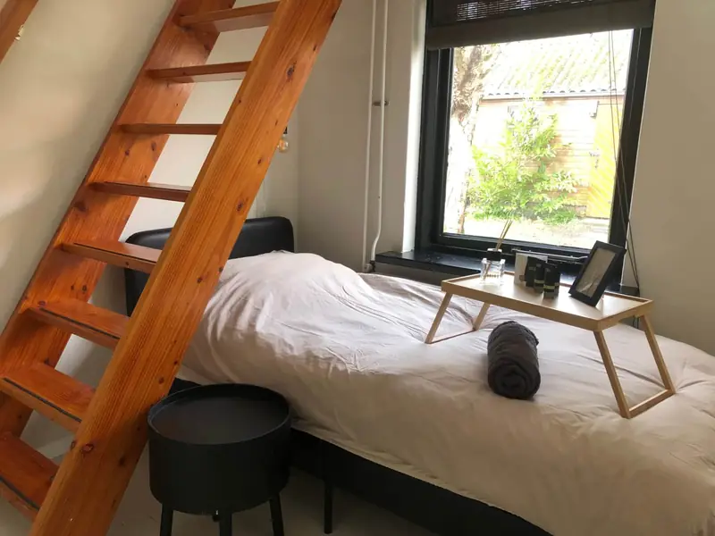 Eenpersoonsbed met een houten trap naar de vliering